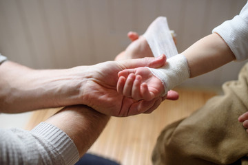 Father putting bandage on small hurt toddler child indoors at home. - obrazy, fototapety, plakaty