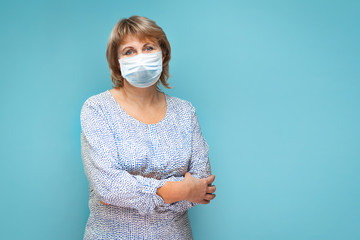 A woman in a medical mask on a blue background looks at the lens.