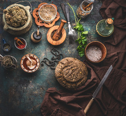 Homemade whole grain bread on dark kitchen table background with knife and cooking tools and ingredients. Top view