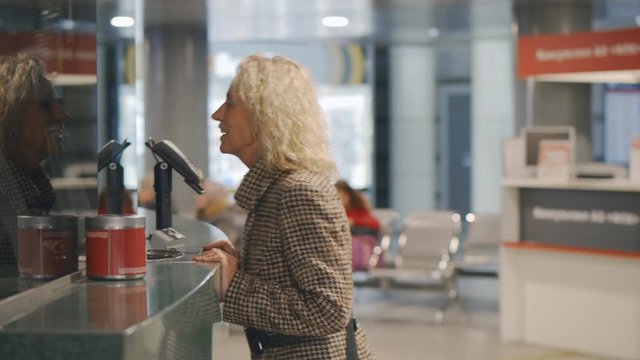 Senior woman buying train ticket in office at railway station