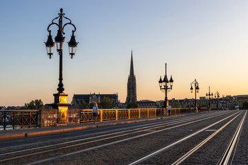 Fototapeta na wymiar Bordeaux, le Pont de Pierre au-dessus de la Garonne, au fond la flèche et la Basilique Saint-Michel de Bordeaux , zone classée au Patrimoine Mondial de l'UNESCO