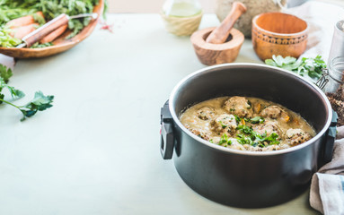 Cooking pot with buckwheat balls in creme sauce standing on kitchen table with herbs and ingredients. Healthy home food cooking