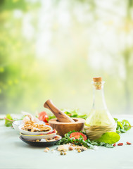 Fresh salad ingredients standing on light table at summer nature background. Olives oil, nuts and seeds, salad leaves, herbs and spices. Healthy food concept. Summer cuisine.