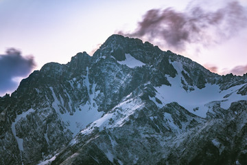 Obraz premium High mountains with snowy peaks at sunset in clouds and fog