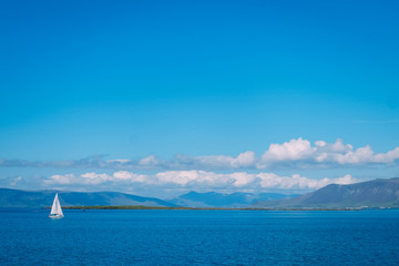 white yacht with a white sail in the distance in the Reykjavik fjord on a sunny summer day and a lot of clouds