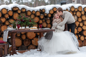 Groom is tenderly hugs his bride from the back on background of winter wedding decoration