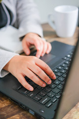 Close up shots of young woman typing on laptop keyboard while working at brown wooden table. Elevated view with selective focus on hand.