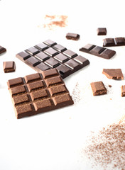 pieces of black and milk chocolate with cocoa powder are scattered on a white background