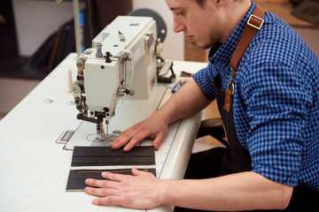 Sewing process of leather product. The man behind white sewing machine. Sewing needle of sewing machine making stitches. A small business of a craftsman.