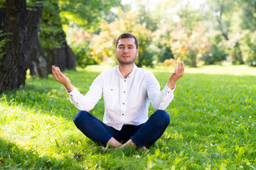 Young man meditates in lotus pose on green grass