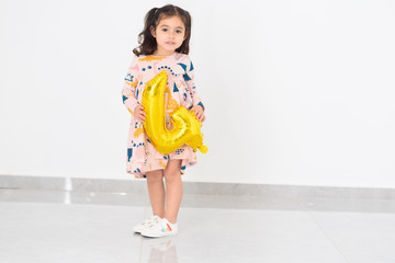 Adorable happy brunette little kid girl celebrating her birthday in home. Little child holding golden balloon 4 number on a white background. 4th Birthday celebration party.