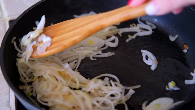 onions fried in the pan with wooden kitchen spatula