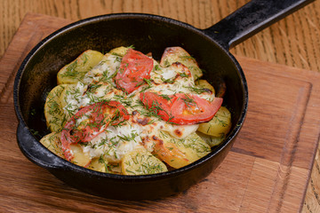 Potato, tomato and onion gratin, with fresh dill served in a pan over rustic wooden background.