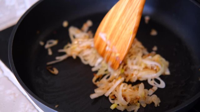 onion fried in the pan with wooden kitchen spatula