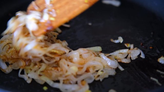 onion fried in the pan with a wooden kitchen spatula