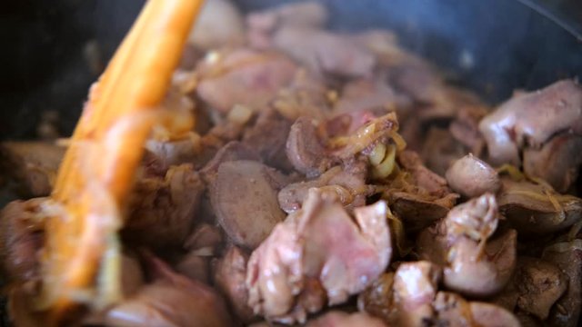chicken liver with onion fried in the pan with a wooden kitchen spatula