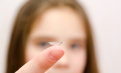 Little girl child putting contact lens into her eye closeup