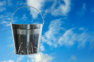 Leaky bucket with water against blue sky. Space for text © New Africa