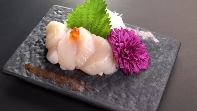 Sliced Japanese food scallop with salmon roe on top sashimi dinner meal on a turn table .