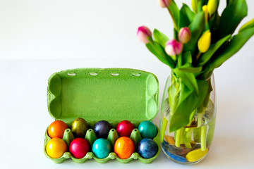 Top view of Beautiful red and yellow tulips with colorful  eggs on white background. Spring and Easter holiday concept with copy space.