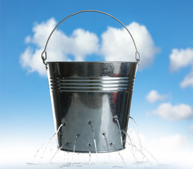 Leaky bucket with water against blue sky