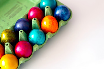 Top view of colorful eggs in the carton box on white background. Easter holiday concept with copy space.