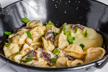 Russian food pelmeni, meat dumplings with mushroom sauce and mashed potatoes in black bowl. Close-up