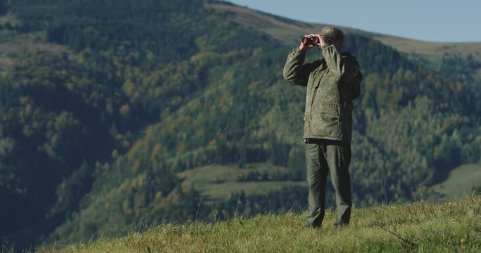 The hunter raised his binoculars, looking for his next destination in the mountains, The general plan