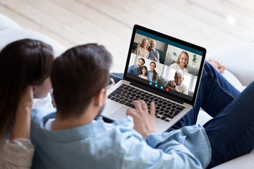Rear back view married couple resting and chatting with relatives via videoconference videocall application, laptop screen view over spouse shoulder. Distant virtual communication, modern tech concept