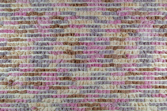 The reverse side of a multi-colored rug, which is a canvas with a white base and horizontal rows of fluffy wool squares of brown, beige, pink and purple colors. Textile background for the design.