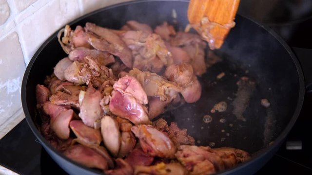 chicken liver with onions fried in a pan with a wooden kitchen spatula