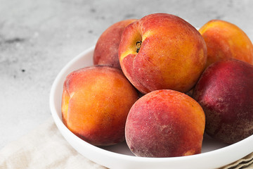 Peaches in a white plate on a light gray table. Close up. Seasonal fruits
