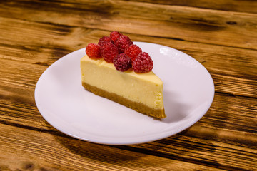 White plate with cheesecake New York and raspberries on wooden table