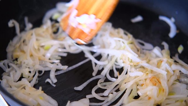 onions fried in the pan with a wooden kitchen spatula