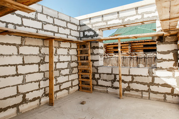 Building site of a house under construction. Unfinished house walls made from white aerated autoclaved concrete blocks. Scaffolding for workers assembled from boards and Euro-pallets.