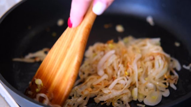 onion fried in the pan with a wooden kitchen spatula