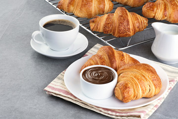 Croissants, chocolate butter, coffee and milk on a gray background.
