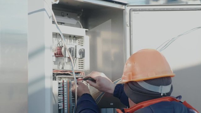 a male electrician works in a switchboard with an electrical connecting cable
