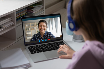 Fototapeta na wymiar Women via videocall talking using webcam pc internet connection, view over girl shoulder. Indian ethnicity teacher share knowledge with learner. Video Conference application, modern tech usage concept