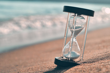 Hourglass at beach coast as time passing concept for business deadline, urgency and running out of time.