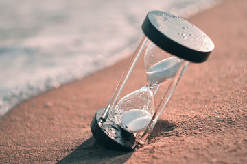 Hourglass at beach coast as time passing concept for business deadline, urgency and running out of...