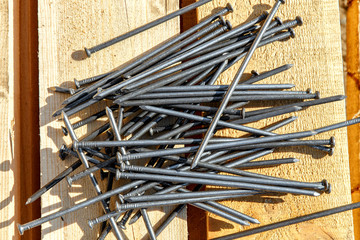 Iron nails on a wooden background. Long, metal, carpenter's nails lie on the lumber for construction. Top view. Flatlay