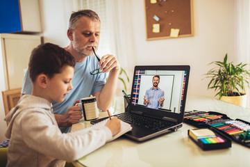 Schoolboy educate online. Father helps his son with home work. Boy in video conference with teacher...