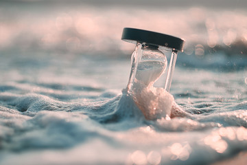 Hourglass at beach coast as time passing concept for business deadline, urgency and running out of...