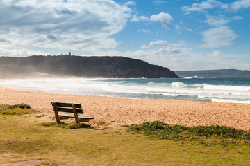 Fototapeta na wymiar Wooden bench on the sandy beach next to the ocean, Atlantic ocean. Palm Beach, Sydney.