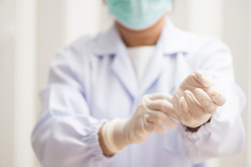 Woman doctor putting white latex medical gloves on white wall background.Surgeon wearing gloves before surgery at operating room.Risk management protection health care concept.