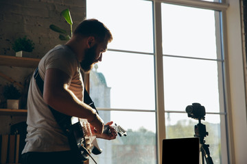 Caucasian musician playing guitar during online concert at home isolated and quarantined. Using camera, laptop, streaming, recording courses. Concept of art, support, music, hobby, education.