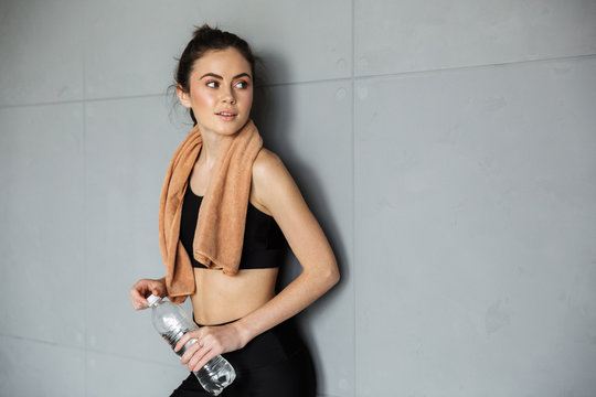 Photo of pleased woman posing with towel over her neck and water bottle