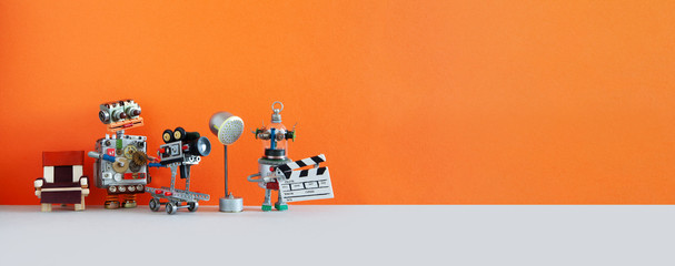 Robotic filmmaking backstage. Two robots shoots motion picture television episode or movie. Funny filmmakers director cameraman, cyborg assistant with clapperboard. Orange gray background, copy space