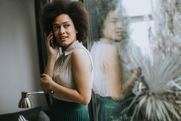 Pretty young woman using mobile phone by the window at home